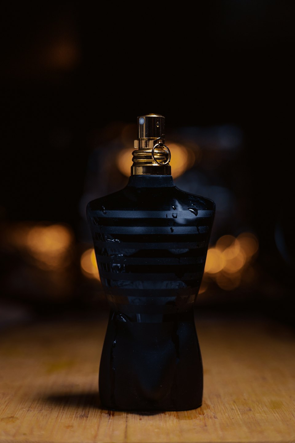 Striped perfume bottle with water droplets on a wooden table.