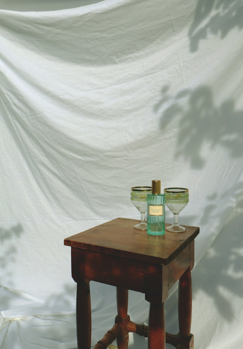 Light blue perfume bottle between two gold-rimmed glasses on wood table.