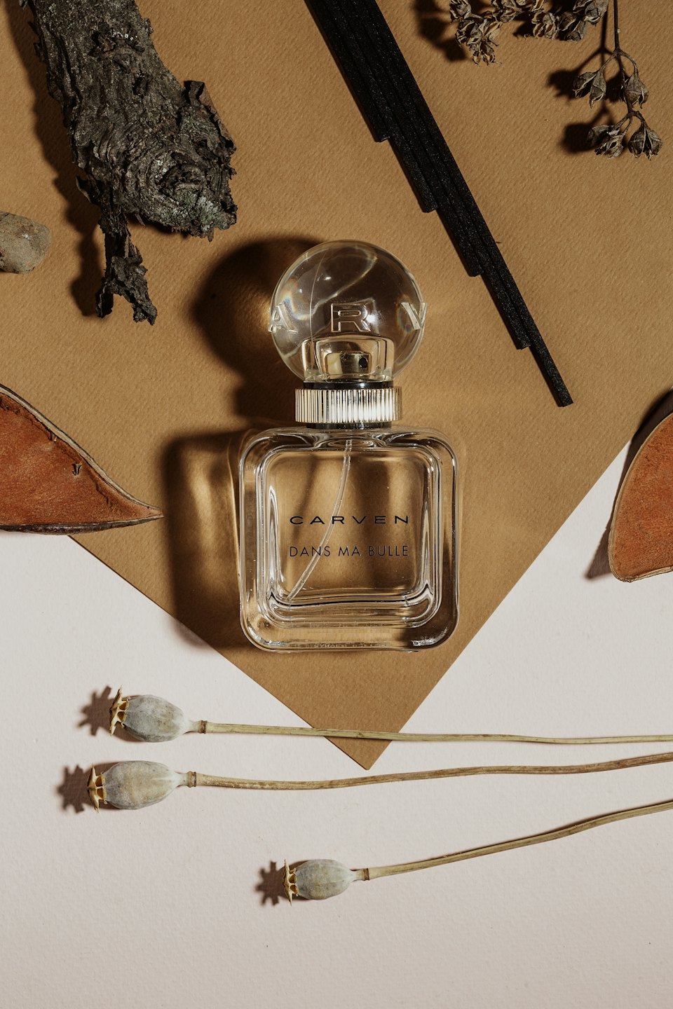 Glass perfume bottle with diffuser reeds and poppy pods.